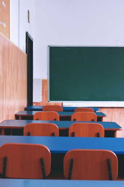 A serene view of an empty classroom with wooden desks, chairs, and a green chalkboard, capturing a quiet educational atmosphere.